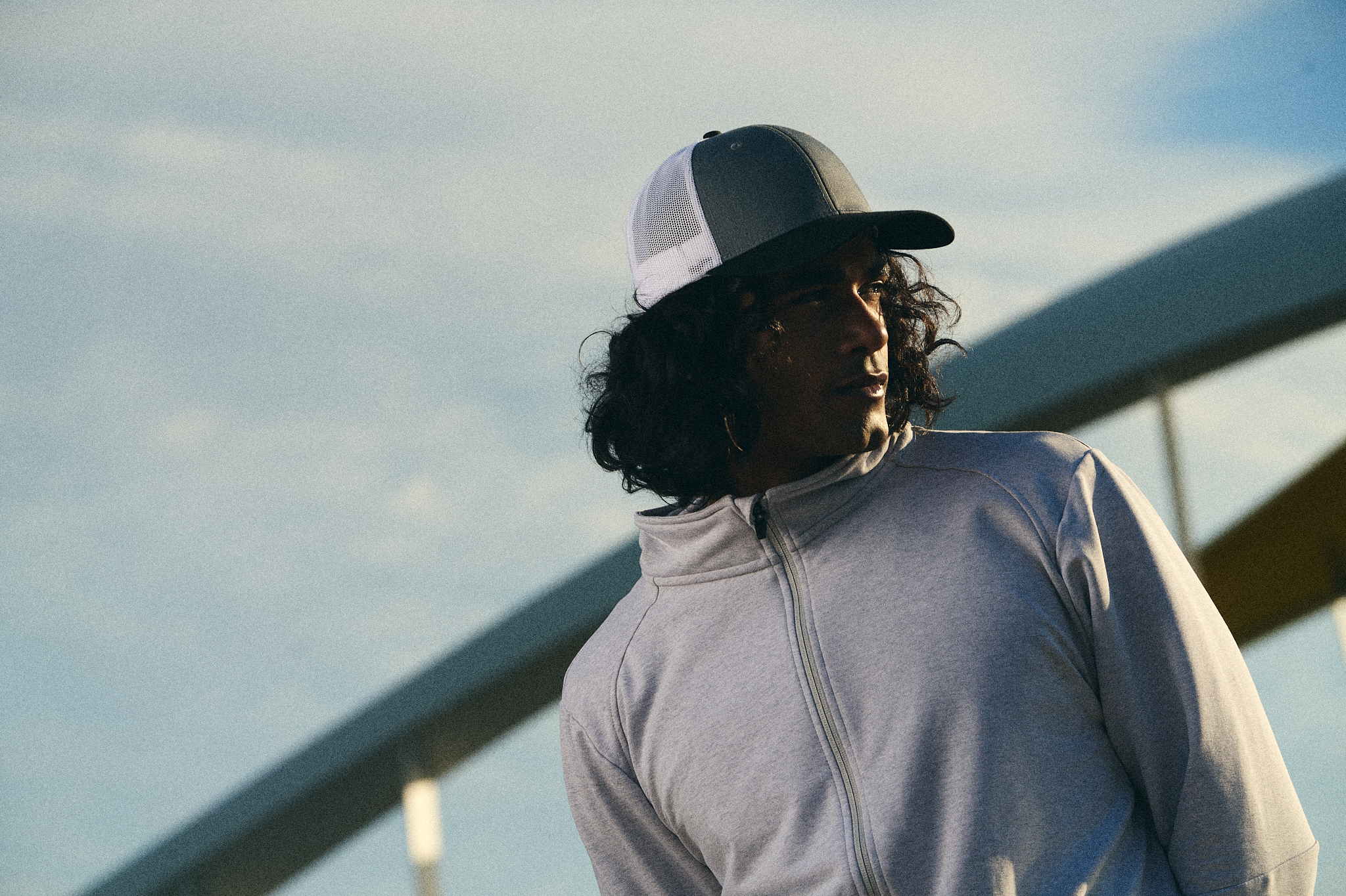 24/7 grey zip sweatshirt and trucker cap worn against open sky - on-location editorial by Fisheye Studio Toronto