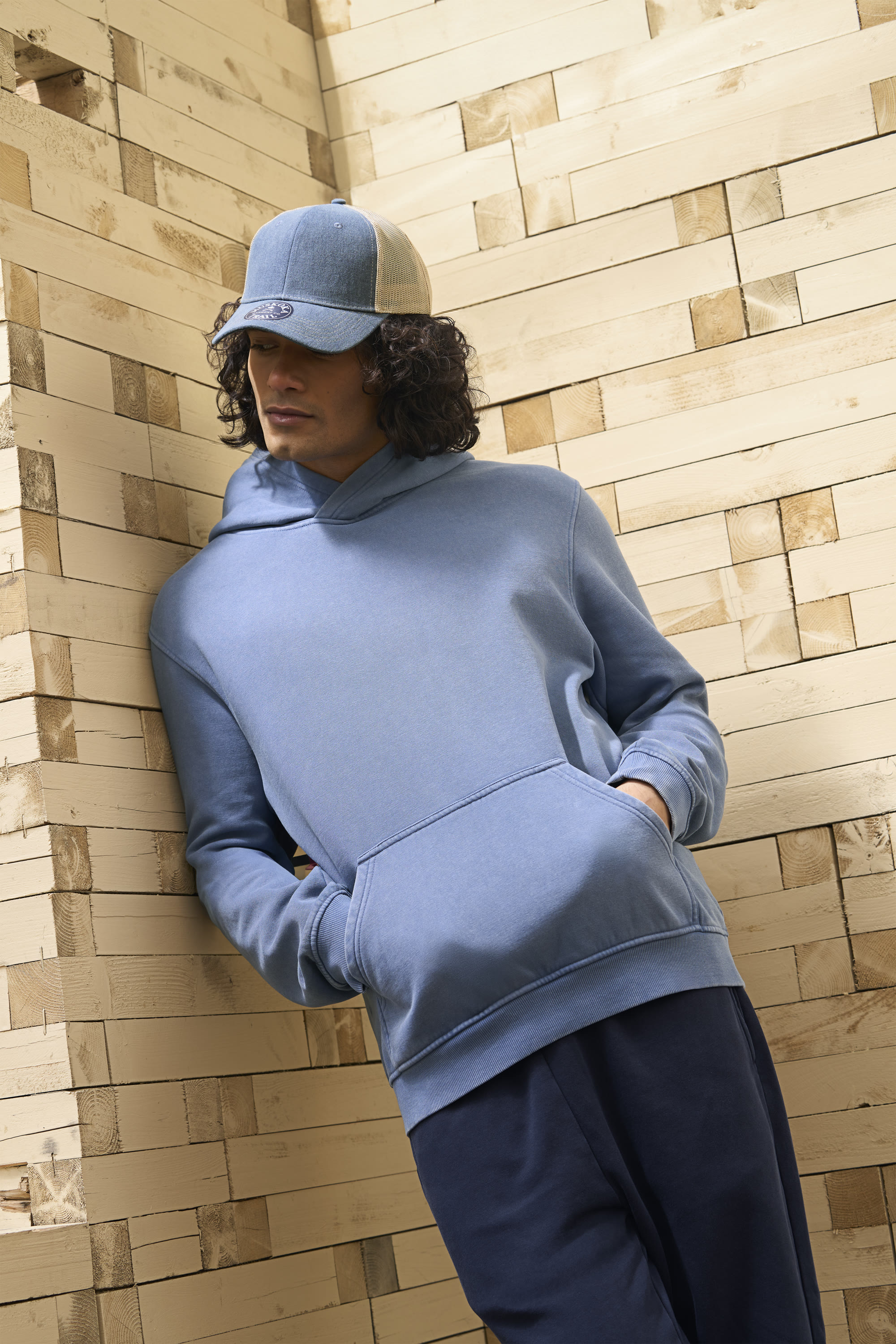 Model in a light blue Canada Sportswear zip hoodie and cap leaning against a stacked timber wall - on-location editorial by Fisheye Studio Toronto